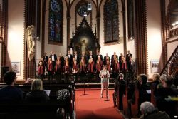Kreiskantorin Beate Kruppe (vorne) führte kompetent und kurzweilig durch die "Nacht der Chöre". Mit von der Partie (auf der Bühne) auch der Chor der Ev. Kirchengemeinde Mahlsdorf-Süd unter Leitung von Bernhard Farenholtz. Foto: Jürgen Bosenius / kklios